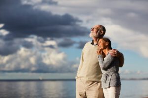 starsze małżeństwo w objęciach patrzące w niebo na tle morza